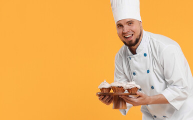 Happy professional confectioner in uniform holding delicious cupcakes on yellow background. Space...