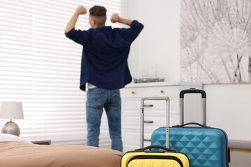 Guest stretching in stylish hotel room, focus on suitcases
