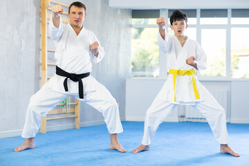 Active middle-aged and teenage male attendees of karate classes practicing kata in sports hall
