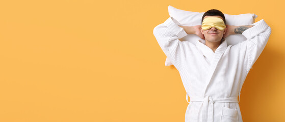 Portrait of handsome young man in bathrobe sleeping on pillow against yellow background