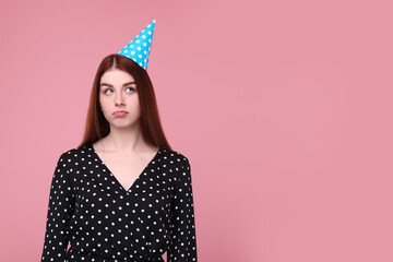 Sad woman in party hat on pink background, space for text