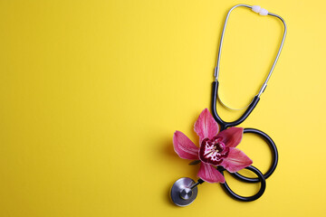 Orchid and stethoscope on a colored background, top view. Symbol of women's health and gynecology.