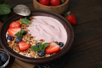Bowl with yogurt, berries and granola on wooden table, closeup. Space for text