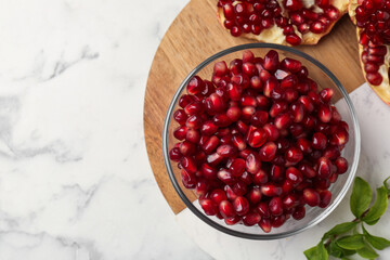 Ripe juicy pomegranate grains and green leaves on white marble table, top view. Space for text
