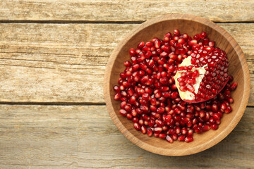 Ripe juicy pomegranate grains in bowl on wooden table, top view. Space for text