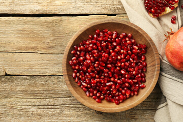 Ripe juicy pomegranate grains in bowl on wooden table, top view. Space for text