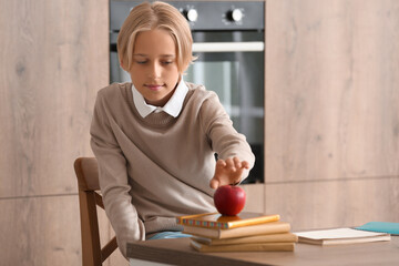 Little boy taking apple while doing homework in kitchen
