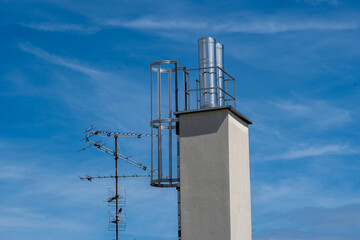 Terrestrial roof antenna with a crow sitting on it and a house chimney in front of a blue sky with...