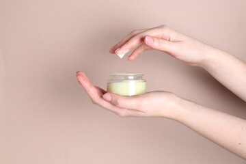 Woman with jar of cream on beige background, closeup