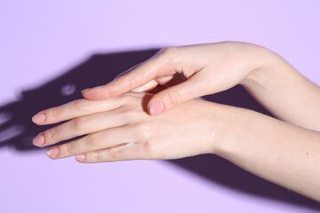 Fototapeta premium Woman applying cream on her hand against violet background, closeup