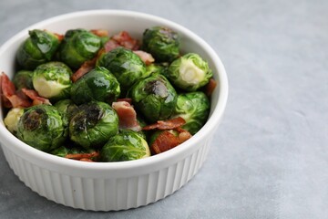 Delicious roasted Brussels sprouts and bacon in bowl on grey table, closeup. Space for text