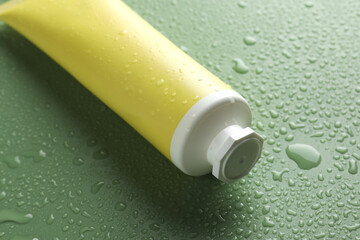 Moisturizing cream in tube on green background with water drops, closeup