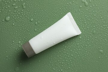 Moisturizing cream in tube on green background with water drops, top view