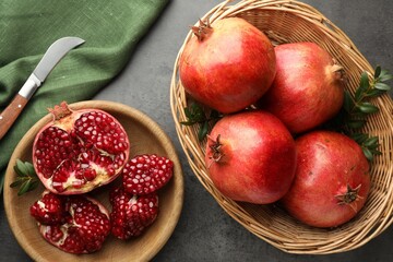 Fresh pomegranates, green leaves and knife on grey table, top view