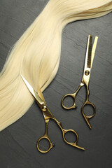 Professional hairdresser scissors with blonde hair strand on dark grey table, flat lay
