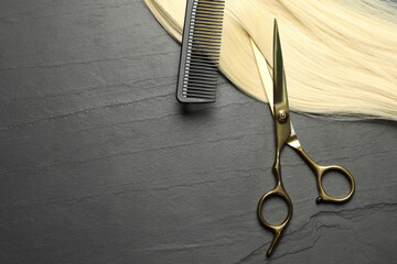Professional hairdresser scissors and comb with blonde hair strand on dark grey table, flat lay....