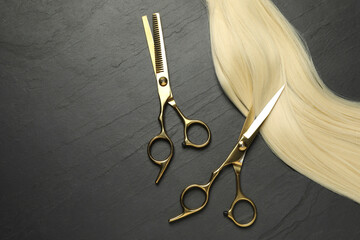 Professional hairdresser scissors with blonde hair strand on dark grey table, flat lay. Space for text