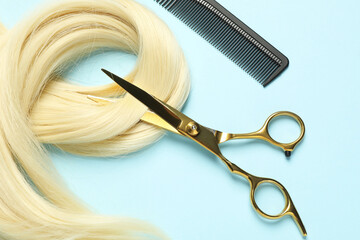 Professional hairdresser scissors and comb with blonde hair strand on light blue background, flat...