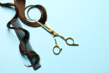 Professional hairdresser scissors and comb with brown hair strand on light blue background, flat...