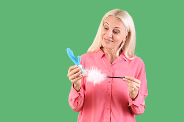 Mature woman with vibrator and feather stick on green background