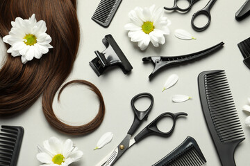 Flat lay composition with professional hairdresser tools, flowers and brown hair strand on light...