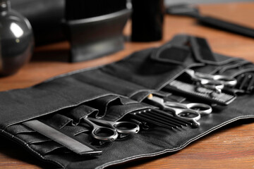 Hairdresser tools. Professional scissors and combs in leather organizer on wooden table, closeup