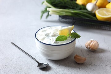 Delicious yogurt with dill in bowl, garlic and spoon on light textured table
