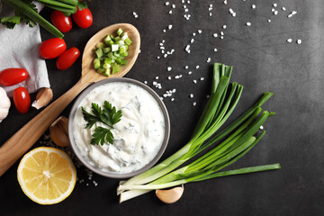Delicious yogurt in bowl and ingredients on black table, flat lay