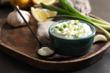 Delicious yogurt in bowl, green onion, garlic and spoon on table, closeup