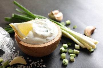 Delicious yogurt in bowl, green onion, garlic and salt on black table, closeup