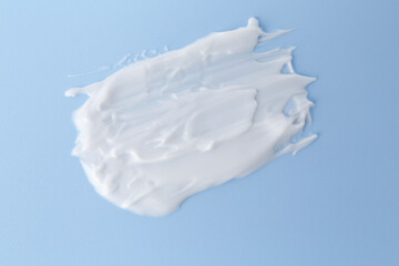 Sample of body care cream on light blue background, top view