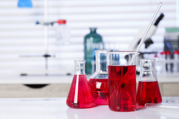 Laboratory analysis. Different glassware with red liquid on white table indoors. Space for text