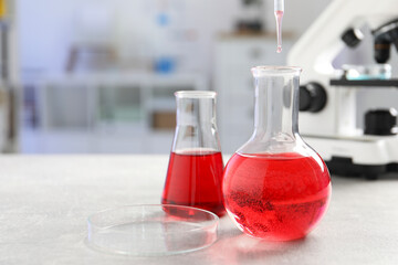 Laboratory analysis. Dripping red liquid into flask at light grey table, closeup. Space for text