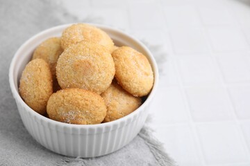 Tasty sugar cookies in bowl on white tiled table, closeup. Space for text