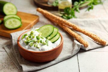 Delicious yogurt, green onion, cucumbers and grissini on light tiled table, closeup