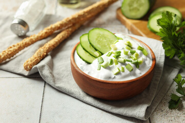 Delicious yogurt with green onion, cucumbers, parsley and grissini on light tiled table, closeup