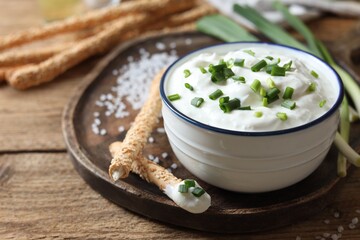 Delicious yogurt, green onion, grissini and salt on wooden table, closeup
