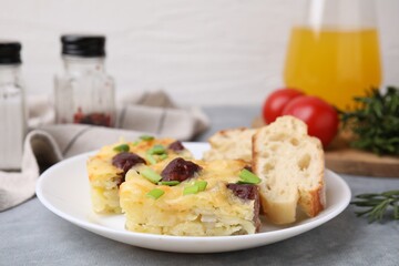 Tasty sausage casserole with green onion and bread on grey table, closeup