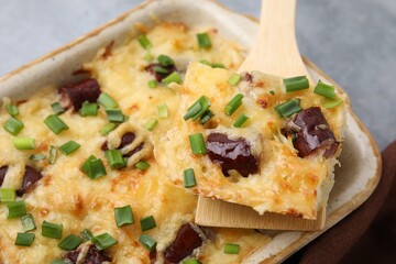 Taking piece of tasty sausage casserole from baking dish at table, closeup