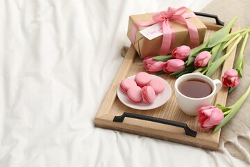 Tasty breakfast served in bed. Delicious macarons, tea, flowers, gift box and card with phrase I Love You on tray, space for text