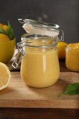 Delicious lemon curd in glass jars, fresh citrus fruit and green leaf on wooden table