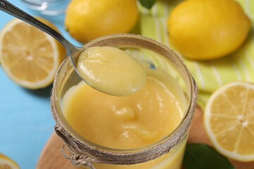 Taking delicious lemon curd from jar at light blue table, closeup