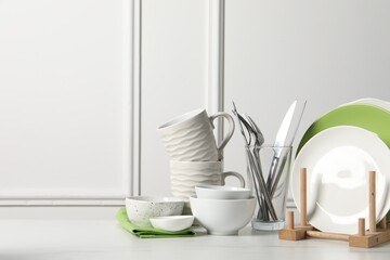 Beautiful ceramic dishware, cups and cutlery on white marble table, space for text