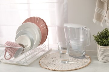 Drainer with different clean dishware, cup, glass and filter jug on light table indoors