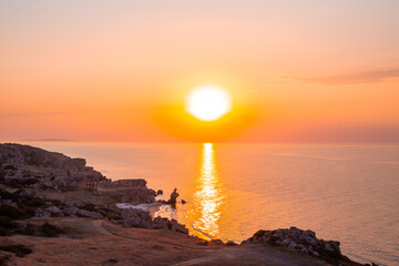 Beautiful seascape. Sunset into the sea with a rocky shore, view from the hill. Wallpaper for the screen