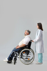 Mature man in wheelchair with nurse on light background