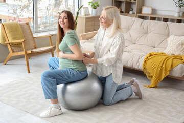 Young pregnant woman with doula training on fitball at home