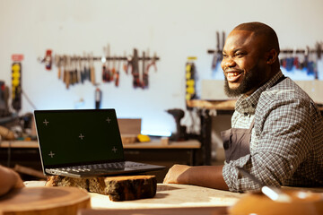 Joyful woodworker and BIPOC coworker using CAD software on green screen laptop to design wooden objects. Cheerful carpenters using program on mockup notebook to plan furniture assembling in joinery