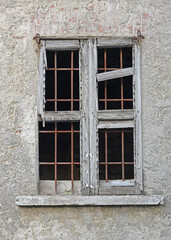 Old, broken, rotten window with rusty bars in weathered plastered brick wall