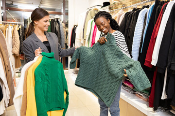 Happy Women Shopping with Consultant Smiling, Choosing Sweaters In A Fashion Store
